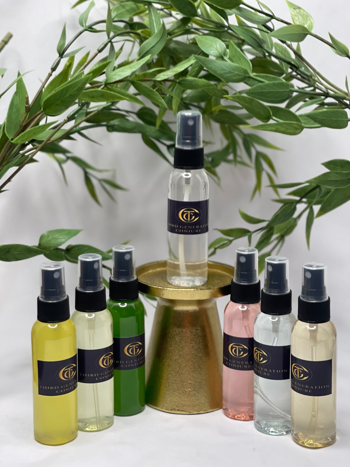 A collection of spray bottles with various colored liquids, arranged in a line with a golden tray. They are labeled with different names such as Protection Mist, Crown of Success, Van Van, Money Drawing, Love Drawing, Road Opener, and Steady Work.